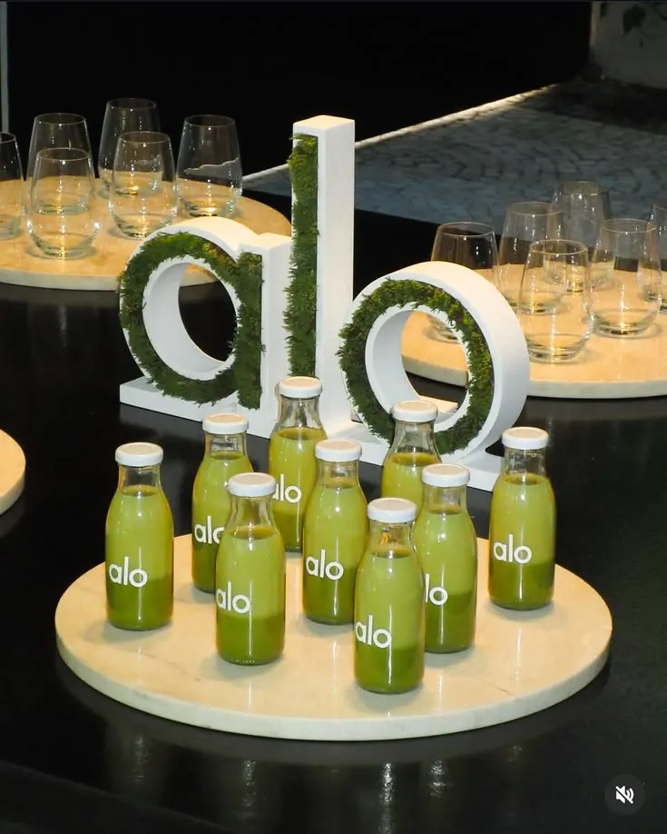 Alo Yoga branded event activation with moss-covered dimensional letters, branded green juice bottles, and marble display