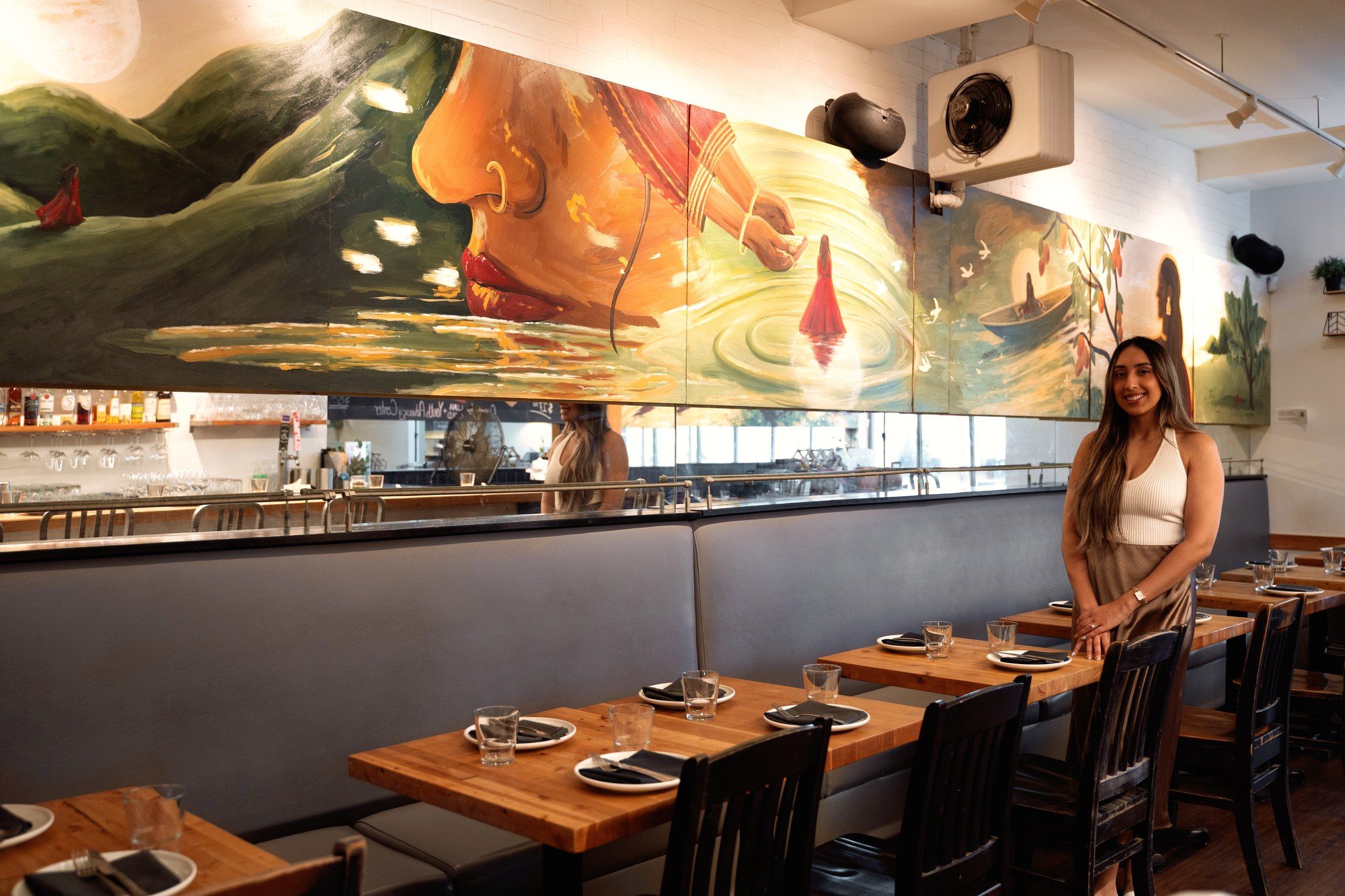 Artist Kiran Rai-Bhullar standing in the UNA Pizza + Wine dining room in front of her painted artboard