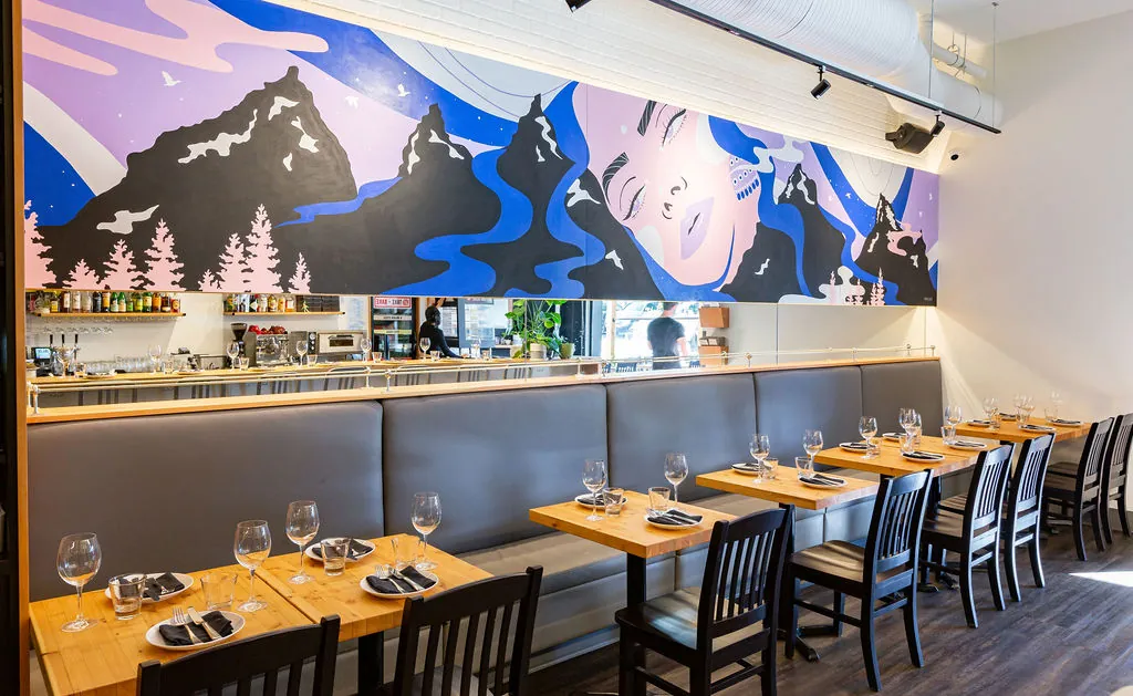 Uprooted mural wide view showing mountain silhouettes, flowing rivers, and pine forest motifs above restaurant banquette seating at UNA Pizza + Wine Bridgeland, KINN Studios Calgary