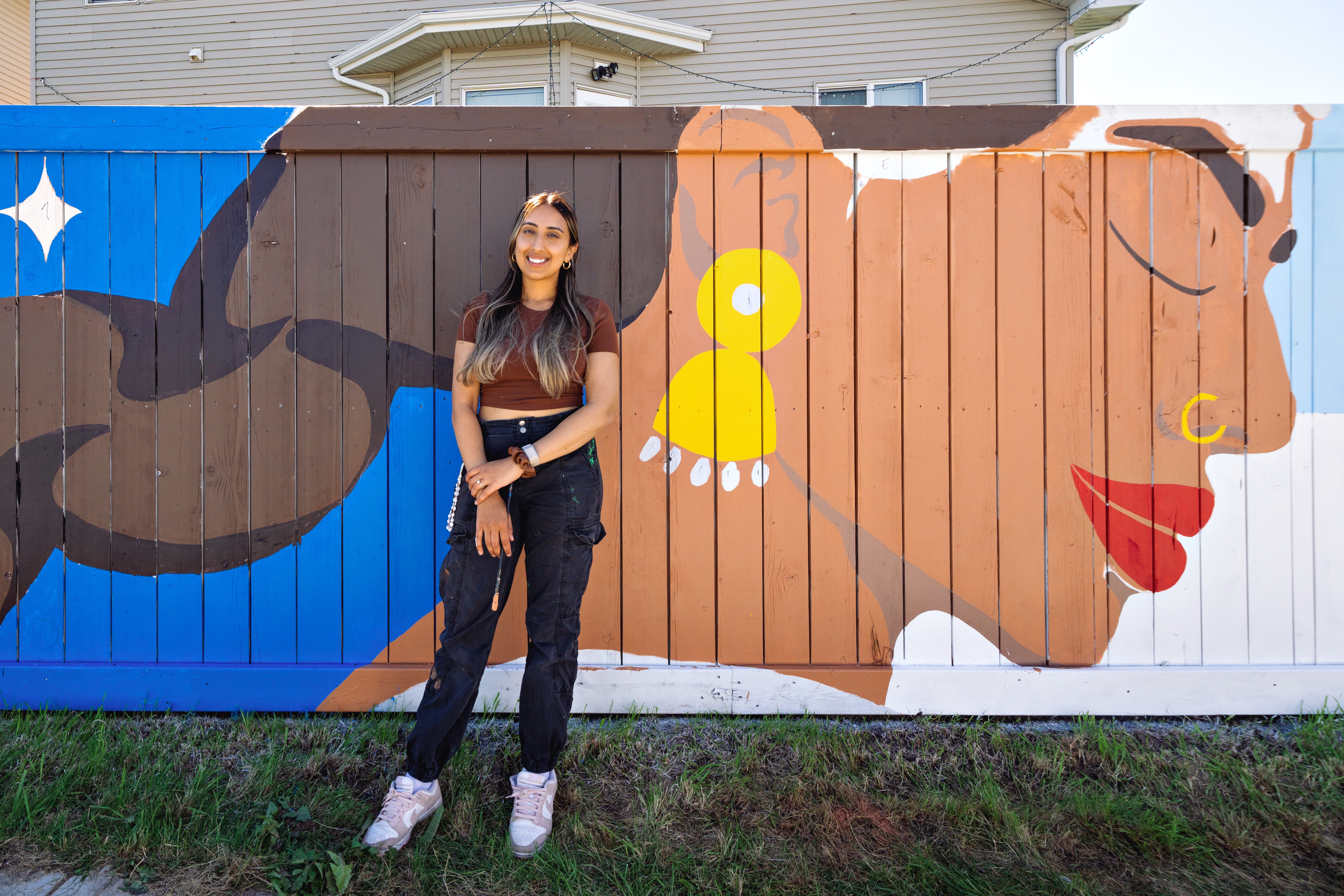 Kiran of KINN Studios standing before a completed section of the Vibrance in Diversity mural, NE Calgary community art project